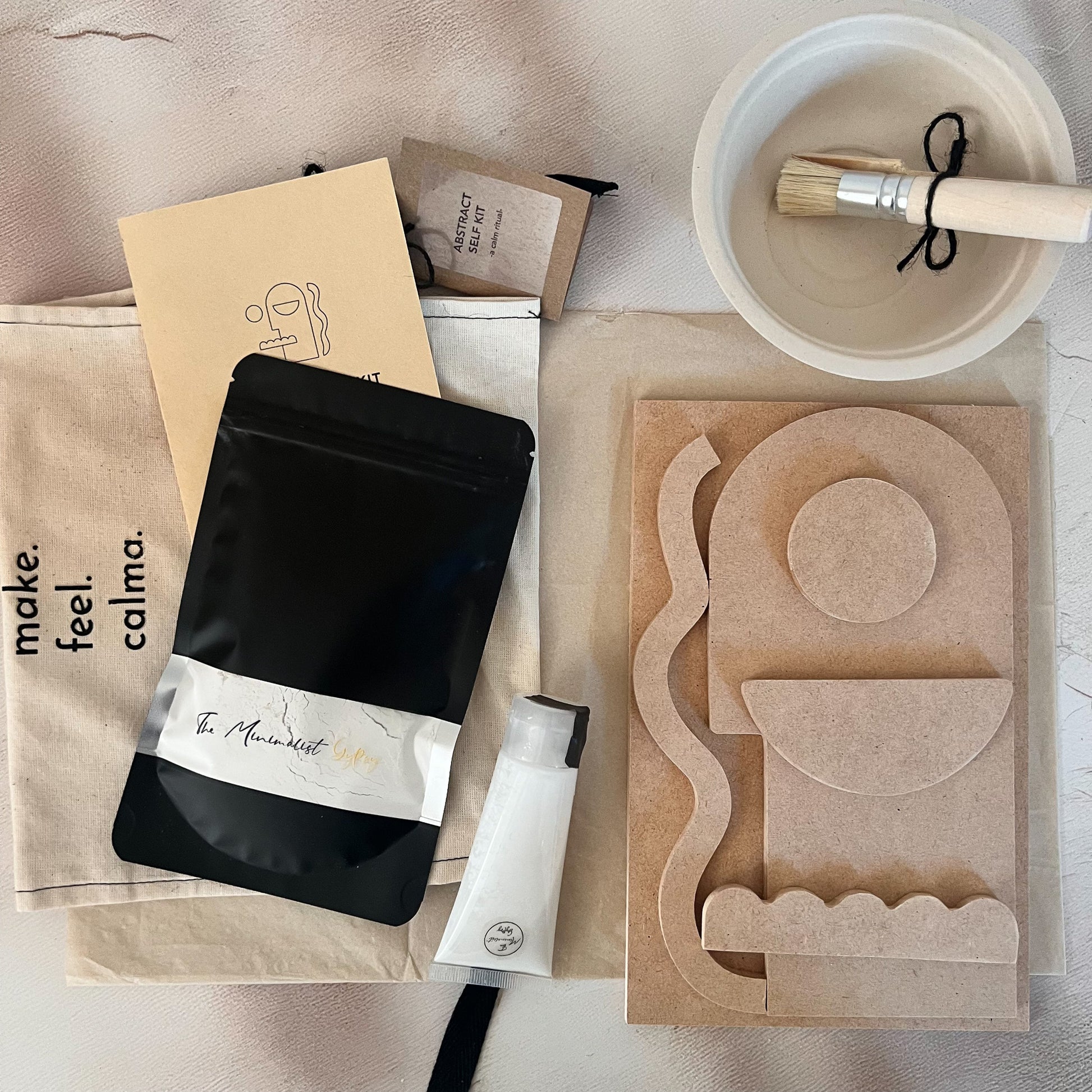 Minimalist plaster DIY kit flat lay with MDF shapes, brush, glue, and packaging — styled on soft neutral fabric.